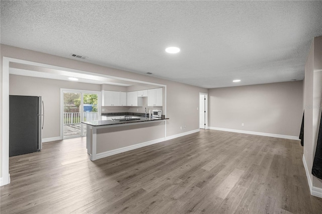 6021 NW 54th Ter, Ocala, FL 34482 - kitchen with freestanding refrigerator, open floor plan, white cabinetry, wood finished floors, and a textured ceiling
