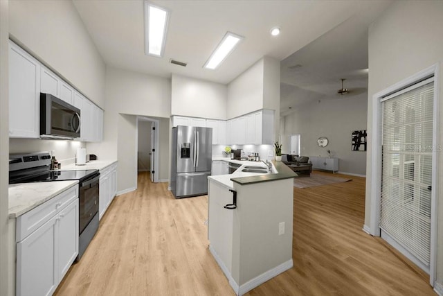3520 NW 46th Ter, Gainesville, FL 32606 - kitchen with stainless steel appliances, light wood-style flooring, high vaulted ceiling, white cabinetry, and a peninsula