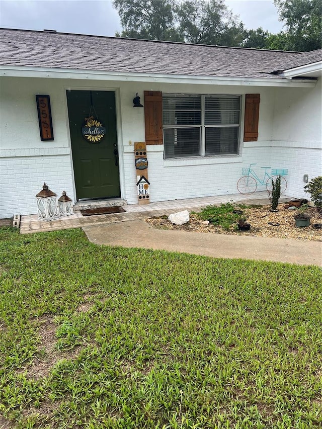 5561 NE 5th Pl, Ocala, FL 34470 - doorway to property featuring brick siding, a porch, a lawn, and a shingled roof