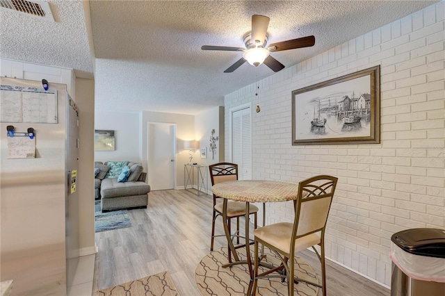 13006 Pebble Beach Cir, Hudson, FL 34667 - dining room featuring a textured ceiling, brick wall, ceiling fan, light wood finished floors, and an accent wall