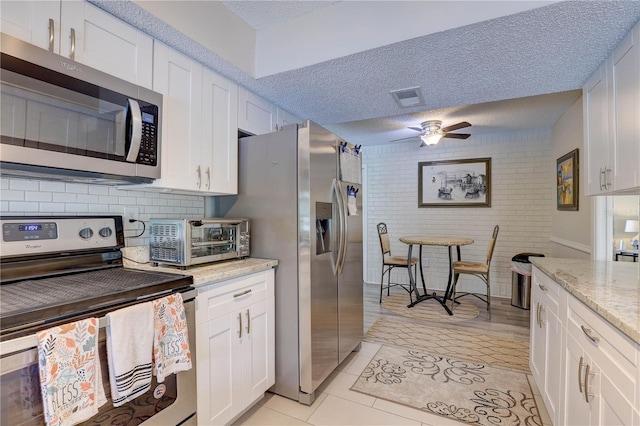 13006 Pebble Beach Cir, Hudson, FL 34667 - kitchen featuring appliances with stainless steel finishes, a ceiling fan, white cabinetry, light tile patterned floors, and a textured ceiling