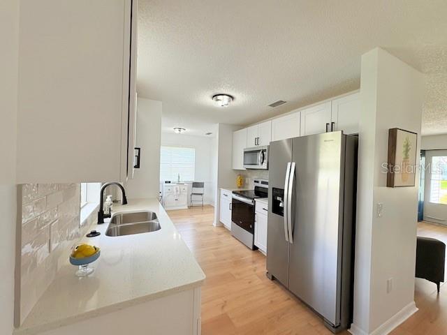 528 Valencia Pl, Lady Lake, FL 32159 - kitchen with stainless steel appliances, light wood finished floors, healthy amount of natural light, white cabinets, and a textured ceiling