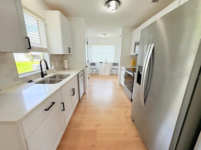 528 Valencia Pl, Lady Lake, FL 32159 - kitchen featuring appliances with stainless steel finishes, light wood-style flooring, decorative backsplash, light countertops, and a textured ceiling