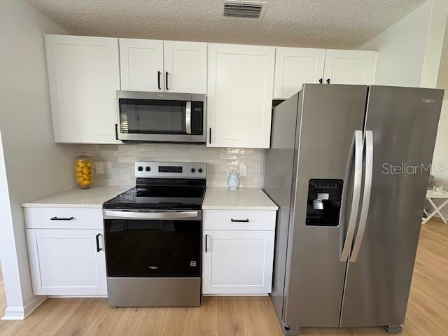 528 Valencia Pl, Lady Lake, FL 32159 - kitchen featuring stainless steel appliances, light wood finished floors, white cabinetry, light countertops, and a textured ceiling