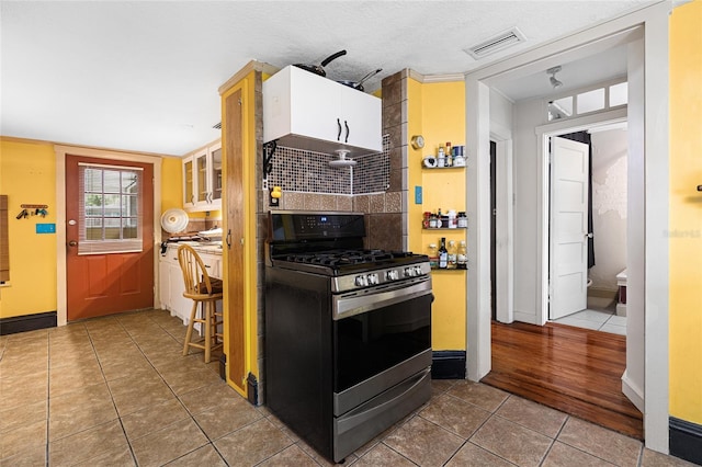 11 62nd St, Yankeetown, FL 34498 - kitchen with stainless steel range with gas stovetop, tile patterned flooring, white cabinetry, backsplash, and glass insert cabinets