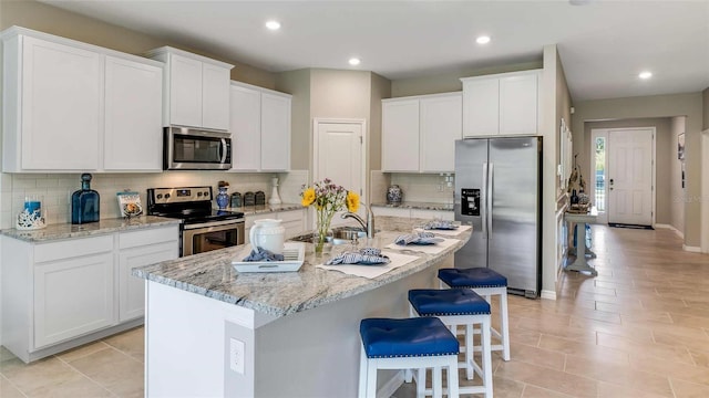4253 SW 54th Street Rd, Ocala, FL 34474 - kitchen featuring appliances with stainless steel finishes, a breakfast bar area, white cabinetry, decorative backsplash, and light stone counters