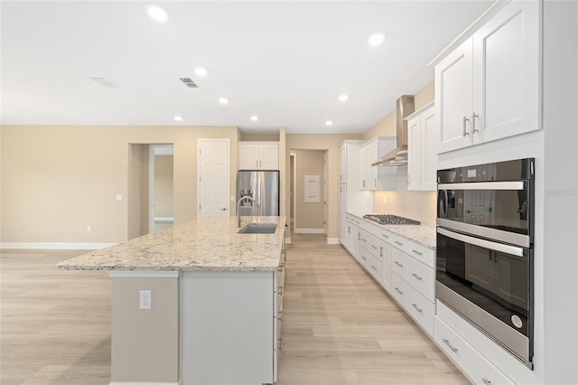 10833 SW 101st Loop, Ocala, FL 34481 - kitchen with appliances with stainless steel finishes, wall chimney exhaust hood, light wood-type flooring, a kitchen island with sink, and white cabinets