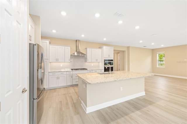10833 SW 101st Loop, Ocala, FL 34481 - kitchen with stainless steel appliances, wall chimney range hood, light wood-style floors, white cabinetry, and a kitchen island with sink