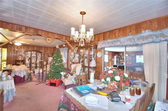 dining space featuring ceiling fan with notable chandelier, carpet floors, and wooden walls