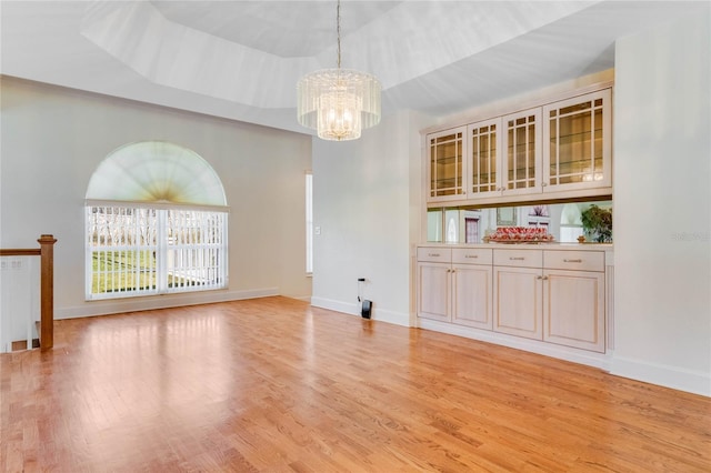 interior space with a tray ceiling, a chandelier, and light hardwood / wood-style flooring