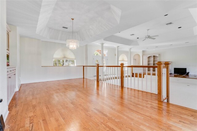 spare room featuring decorative columns, a tray ceiling, ceiling fan with notable chandelier, and light hardwood / wood-style flooring