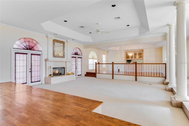 unfurnished living room featuring a multi sided fireplace, a raised ceiling, ceiling fan, decorative columns, and carpet