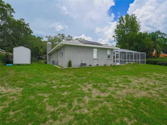 back of property with a yard, central AC, and a storage shed