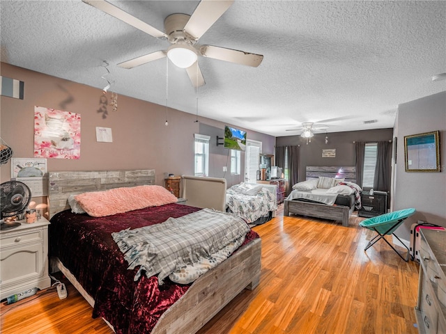 bedroom featuring ceiling fan, light hardwood / wood-style floors, multiple windows, and a textured ceiling
