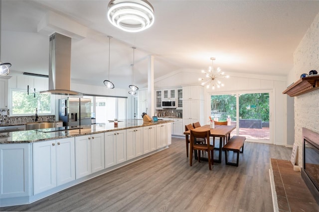 kitchen featuring white cabinetry, decorative light fixtures, dark stone countertops, a chandelier, and island range hood