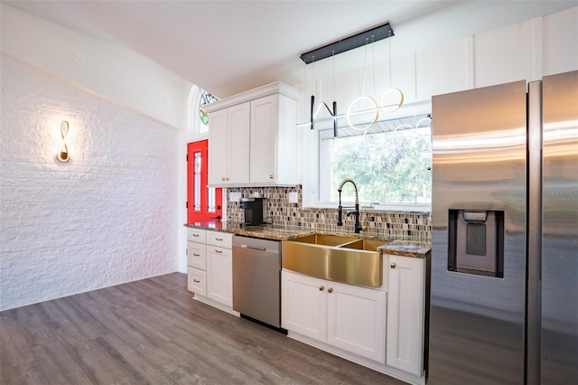 kitchen with dark wood-type flooring, appliances with stainless steel finishes, white cabinets, dark stone countertops, and sink