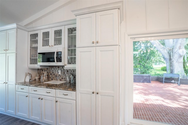 bar with lofted ceiling, tasteful backsplash, dark stone countertops, and white cabinetry