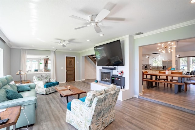 living room featuring ornamental molding, ceiling fan with notable chandelier, and light wood-type flooring