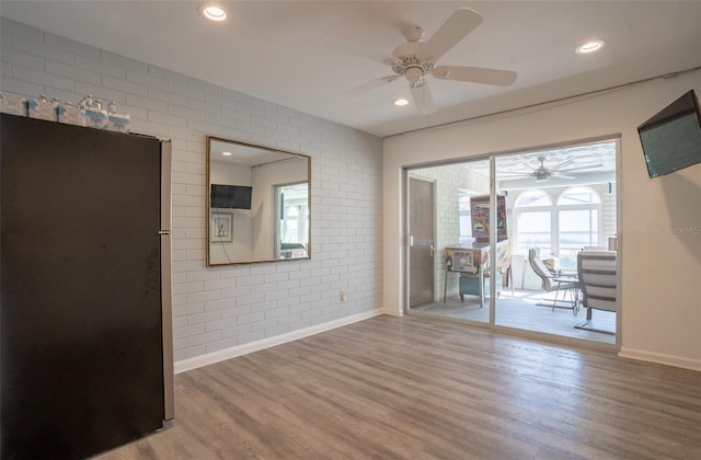 spare room with brick wall, wood-type flooring, and ceiling fan