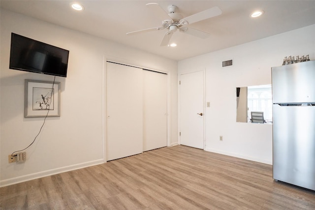 unfurnished bedroom featuring stainless steel fridge, ceiling fan, a closet, and light hardwood / wood-style flooring