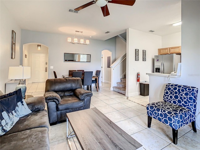 tiled living room with ceiling fan with notable chandelier