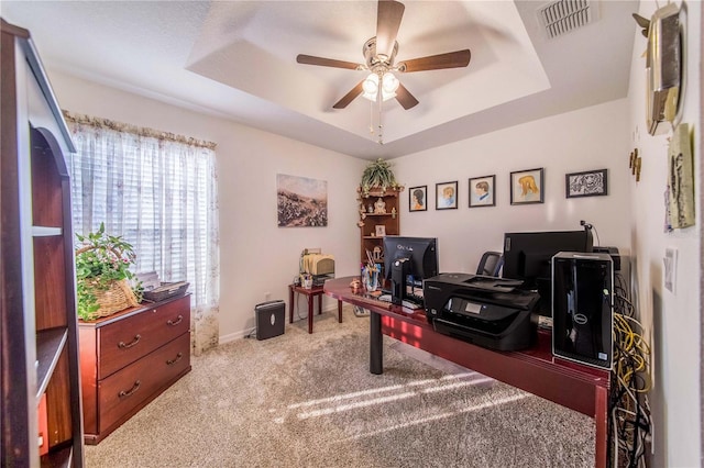 carpeted office with ceiling fan and a tray ceiling