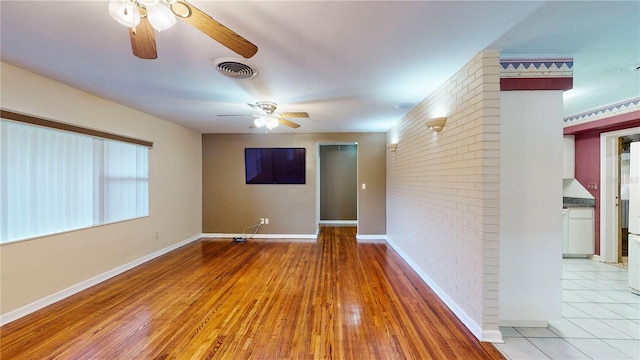 empty room with brick wall, ceiling fan, and hardwood / wood-style flooring