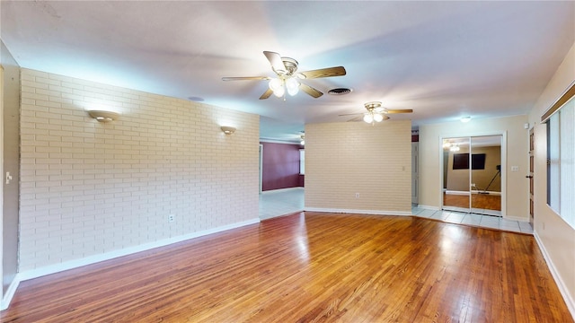 empty room featuring brick wall, ceiling fan, and wood-type flooring