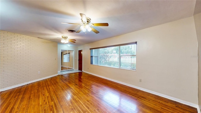 spare room featuring brick wall, ceiling fan, and hardwood / wood-style flooring