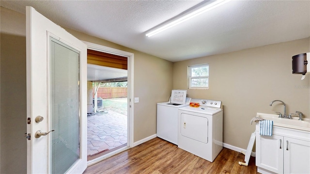 clothes washing area featuring sink, light hardwood / wood-style floors, washer and clothes dryer, and cabinets