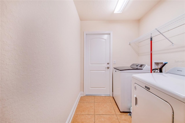 clothes washing area with baseboards, independent washer and dryer, light tile patterned flooring, and laundry area