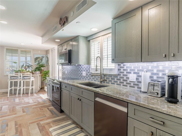 kitchen with decorative backsplash, sink, light parquet floors, light stone countertops, and stainless steel appliances