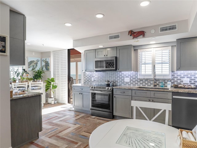 kitchen with light parquet floors, appliances with stainless steel finishes, gray cabinetry, and sink