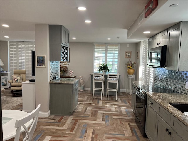 kitchen featuring tasteful backsplash, dark parquet floors, light stone countertops, gray cabinetry, and black / electric stove