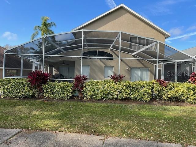 rear view of property featuring stucco siding, a yard, and a lanai