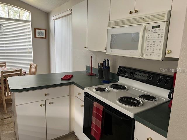 kitchen featuring white microwave, a peninsula, electric range oven, vaulted ceiling, and white cabinets