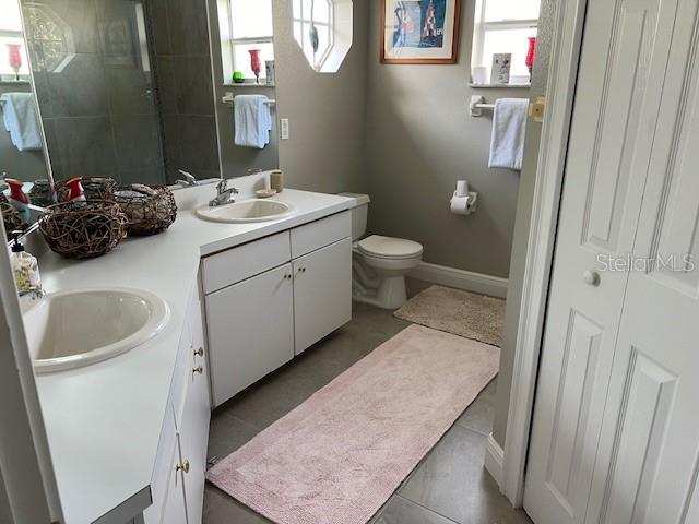 bathroom featuring toilet, tile patterned floors, and dual bowl vanity