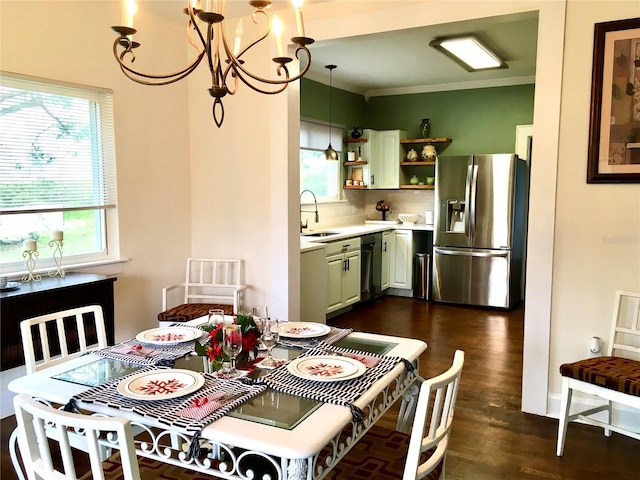 dining area with dark wood-type flooring, ornamental molding, a notable chandelier, and sink