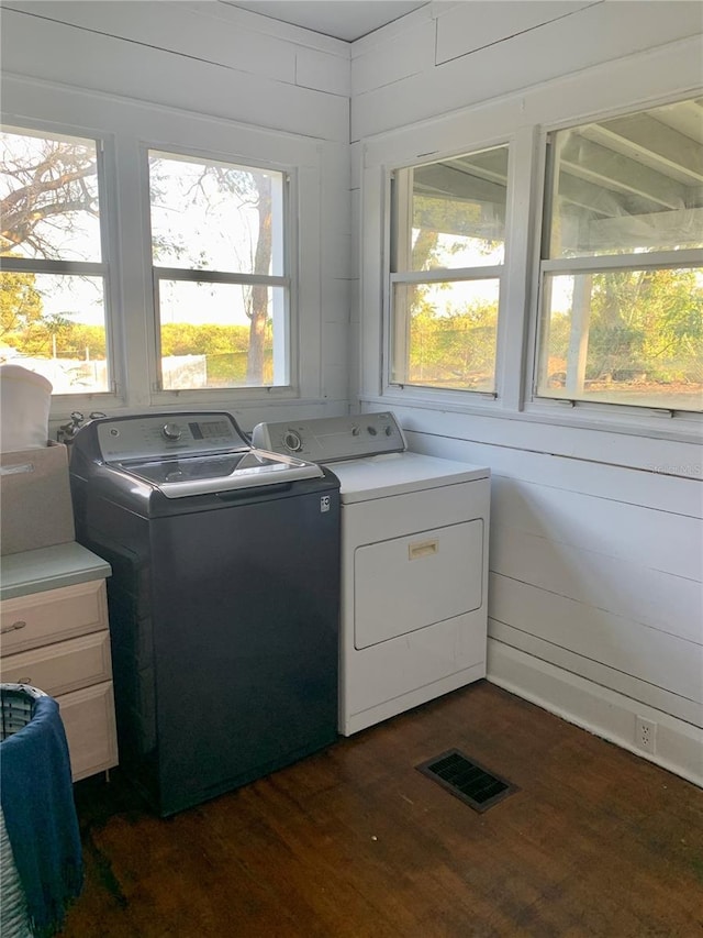 clothes washing area with washer and clothes dryer, wood walls, and dark hardwood / wood-style flooring