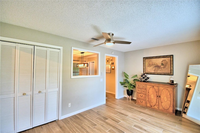 interior space featuring light hardwood / wood-style floors, a closet, a textured ceiling, and ceiling fan with notable chandelier