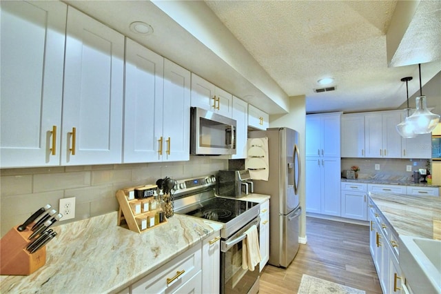 kitchen with light wood-type flooring, light stone countertops, stainless steel appliances, and white cabinetry