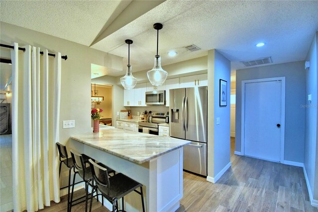 kitchen featuring hanging light fixtures, light hardwood / wood-style floors, stainless steel appliances, white cabinets, and light stone counters