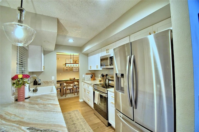 kitchen with decorative light fixtures, appliances with stainless steel finishes, white cabinetry, light wood-type flooring, and sink