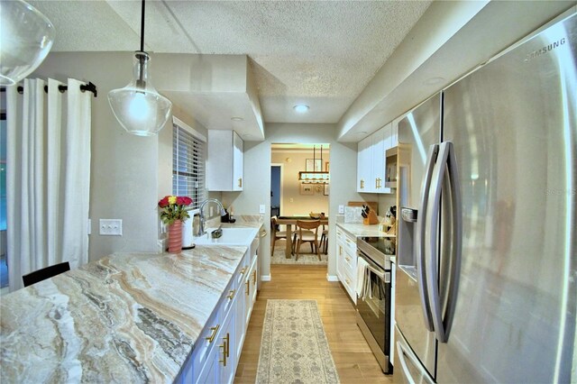 kitchen with white cabinetry, decorative light fixtures, appliances with stainless steel finishes, light wood-type flooring, and light stone counters