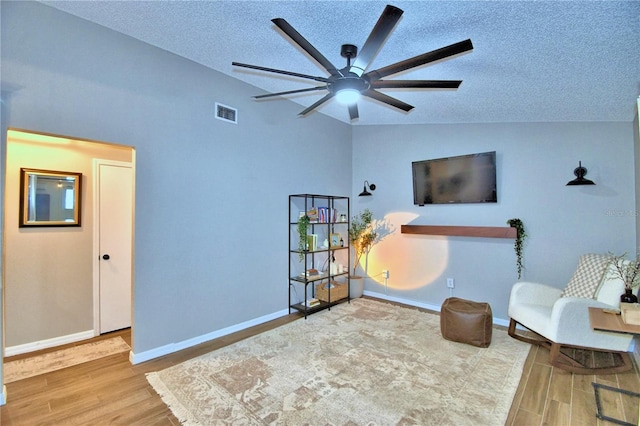 living area featuring a textured ceiling, light hardwood / wood-style floors, ceiling fan, and vaulted ceiling