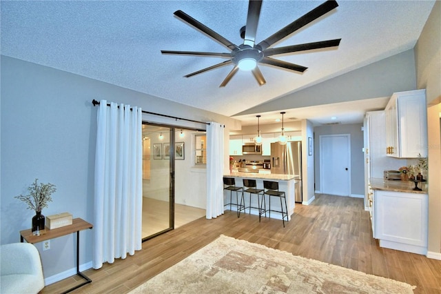 living room featuring vaulted ceiling, light hardwood / wood-style floors, a textured ceiling, and ceiling fan with notable chandelier