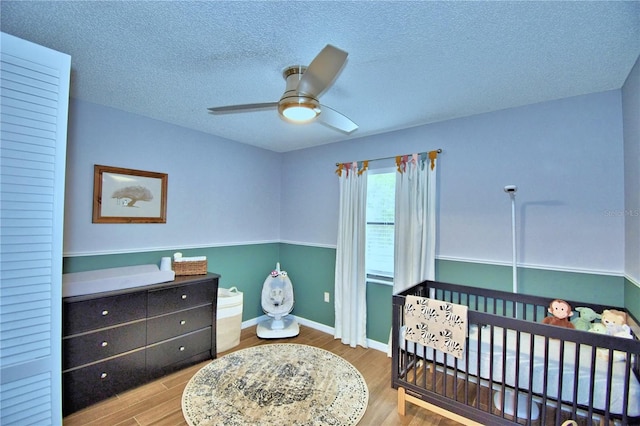 bedroom with a textured ceiling, a crib, ceiling fan, and hardwood / wood-style flooring