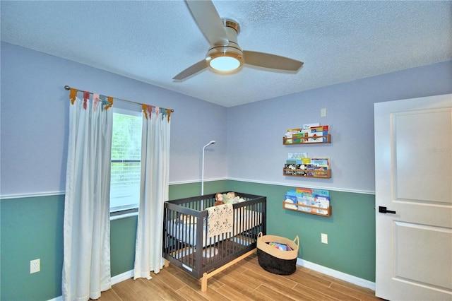bedroom featuring light hardwood / wood-style floors, a crib, ceiling fan, and a textured ceiling