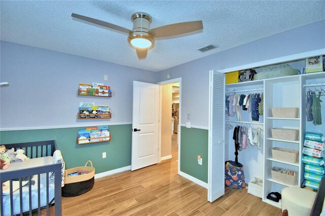 bedroom with a closet, ceiling fan, light wood-type flooring, a textured ceiling, and a nursery area