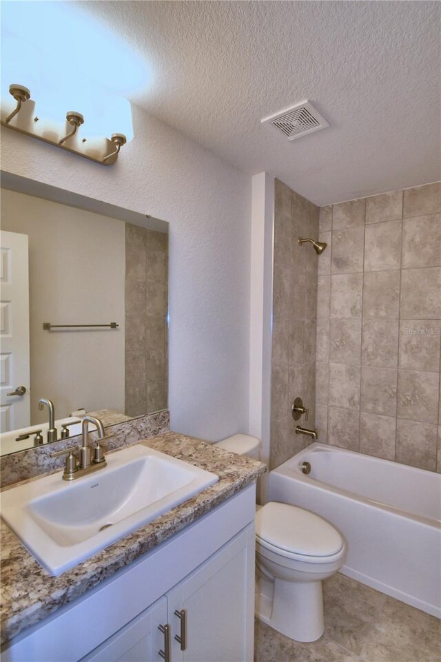 full bathroom with vanity, toilet, a textured ceiling, and tiled shower / bath combo